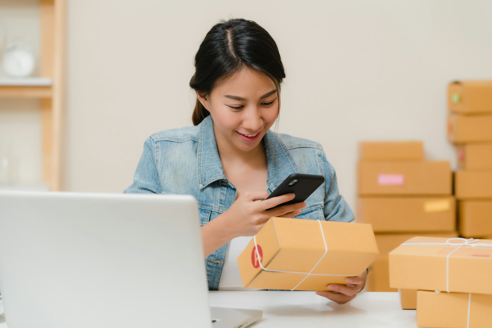 Chủ shop online kiểm tra đơn hàng bằng điện thoại bên cạnh các thùng carton